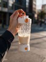 Hand hält den VELORA Volt Akku-Shaker mit frisch gemixtem Shake unterwegs in der Stadt