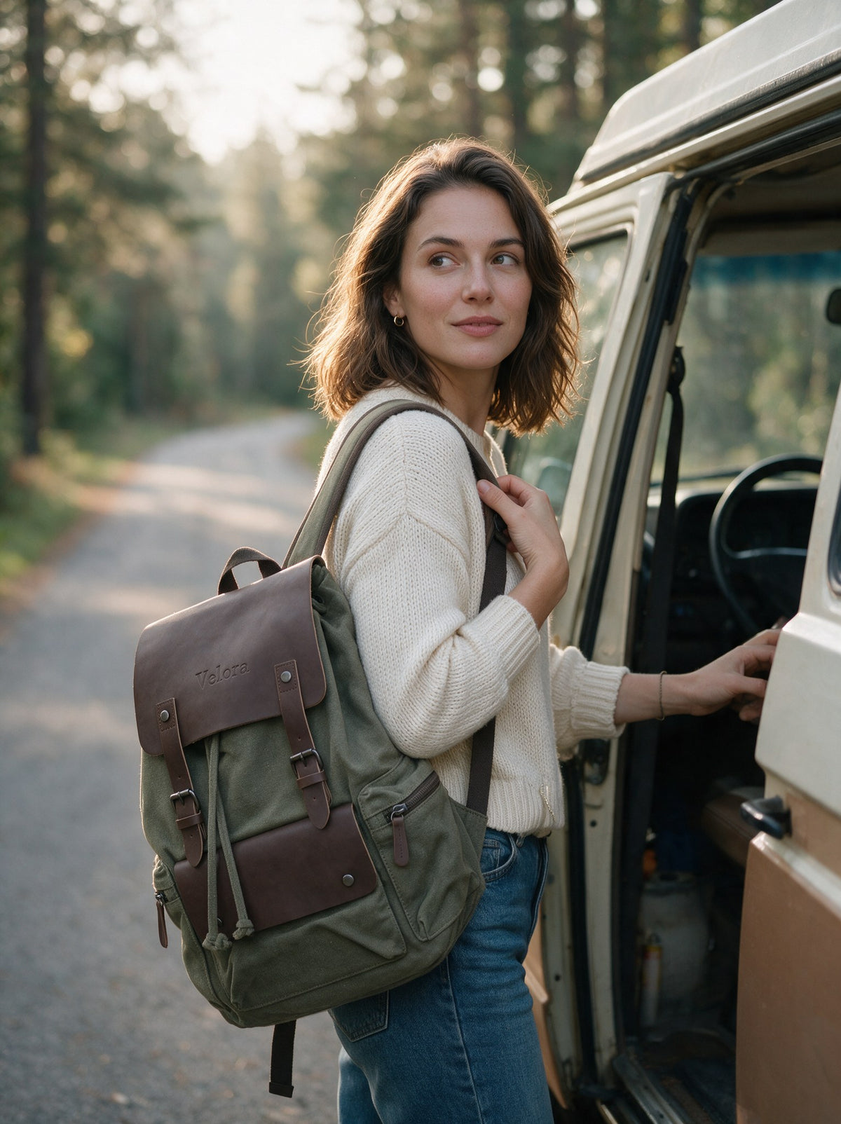 Frau mit dem Vintage Canvas Rucksack über der Schulter steigt an einer Waldstraße in einen Campervan