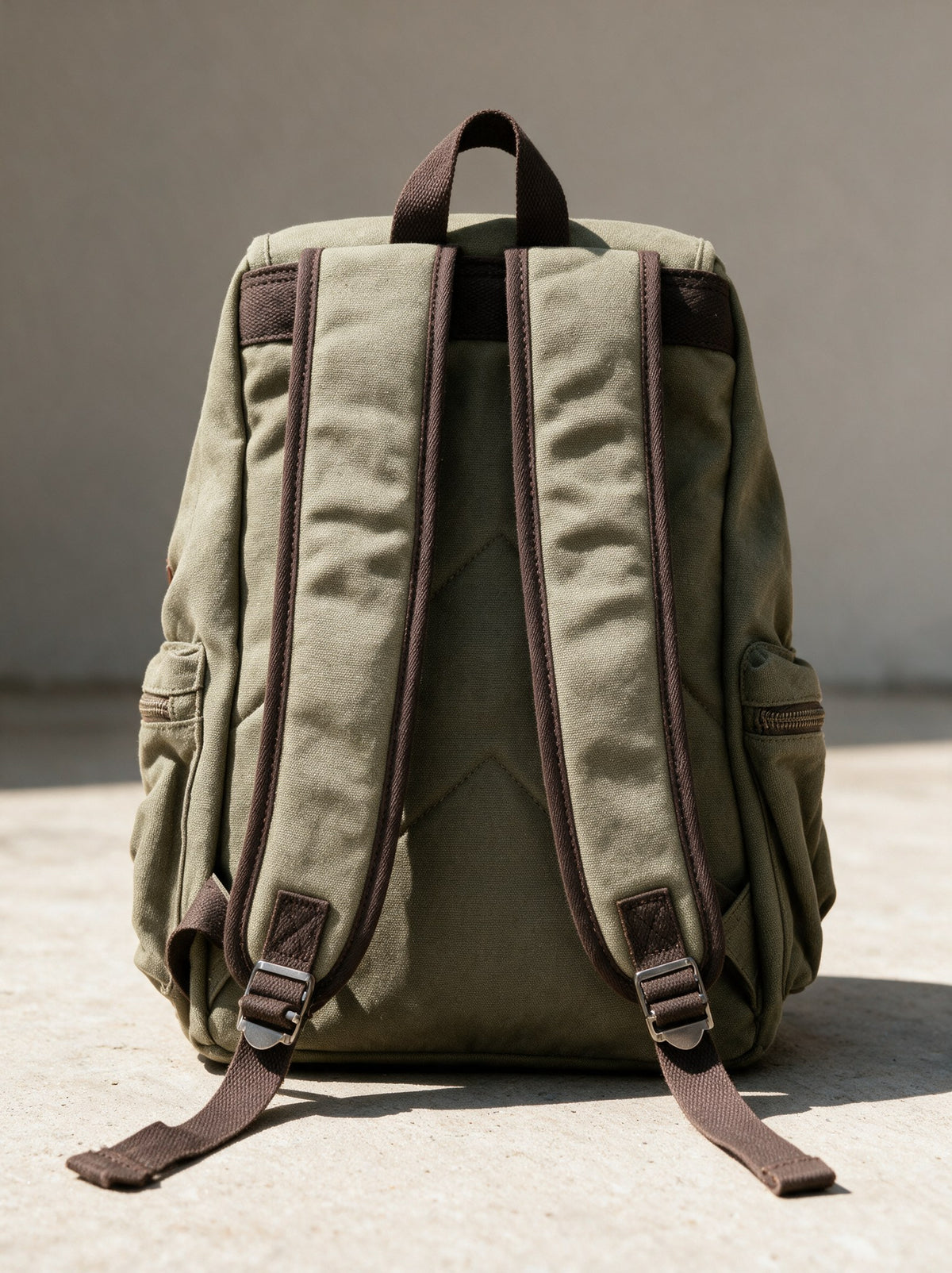 Rückseite des olivgrünen Canvas Rucksacks mit verstellbaren Schulterträgern, Metall-Schiebern und Trageschlaufe oben