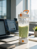 Elektrischer Shaker mit grünem Smoothie auf dem Schreibtisch neben Laptop im Büro